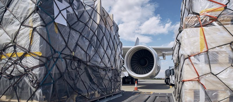 Preparation before flight. Loading of cargo containers against jet engine of freight airplane.